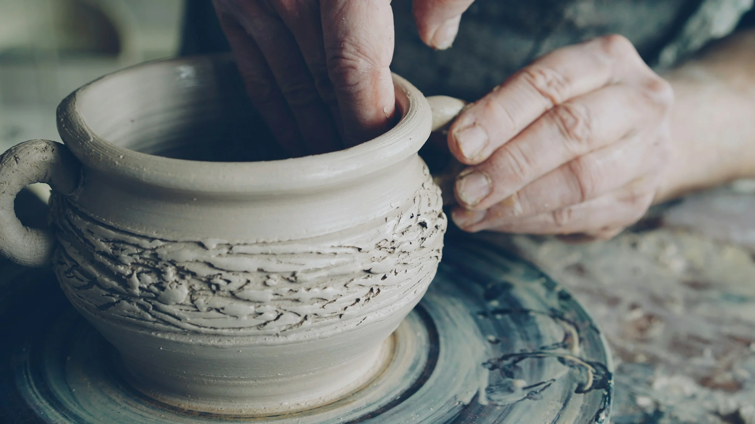 Hands shaping clay on a pottery wheel